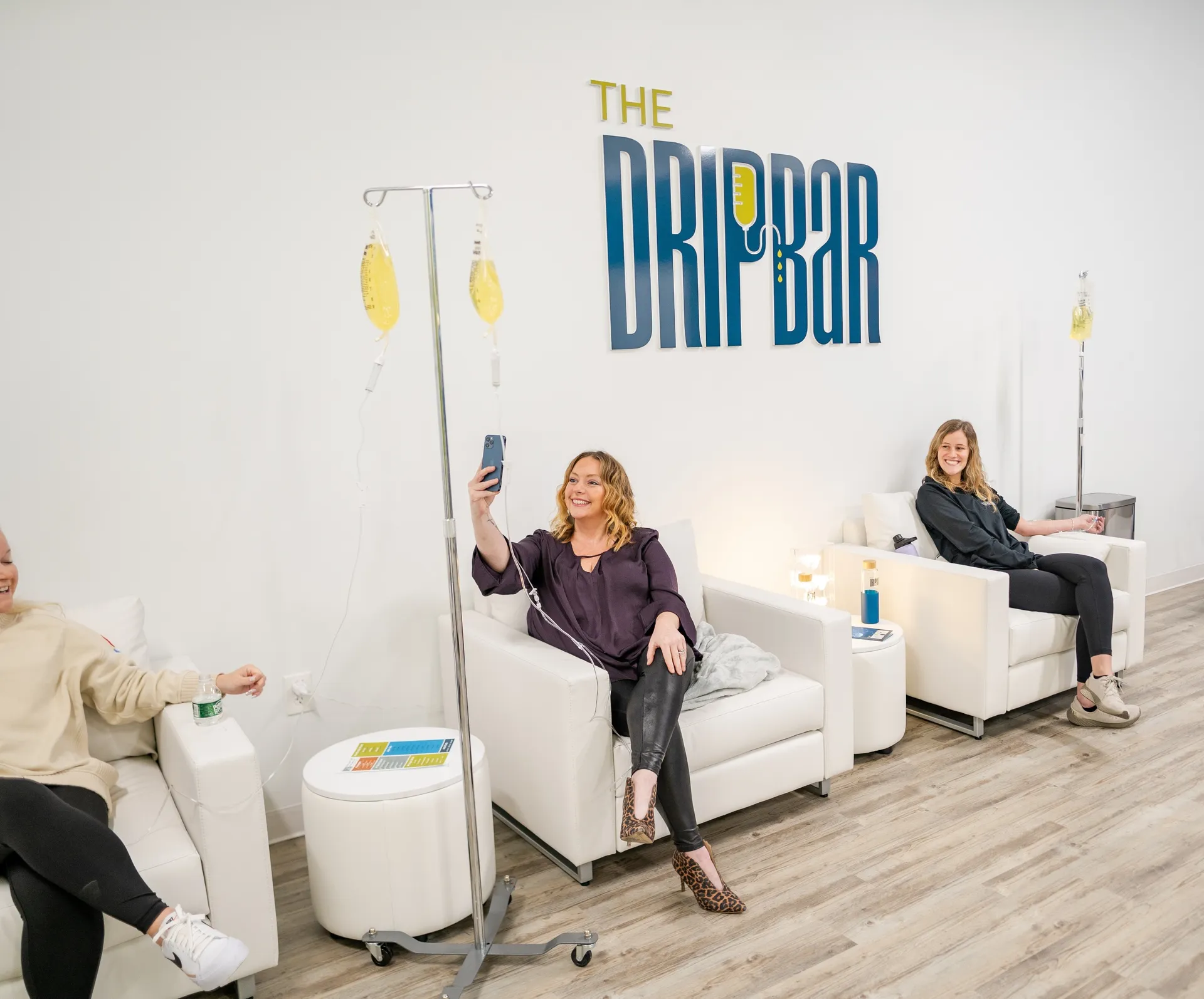 The DRIPBaR logo wall with three clients on white armchairs